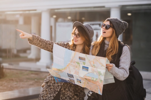 Women with hats walking with friend around city holding a map