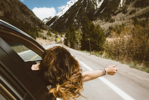 Woman joyfully driving a car, feeling the wind on her face as she extends her arms out of the window.